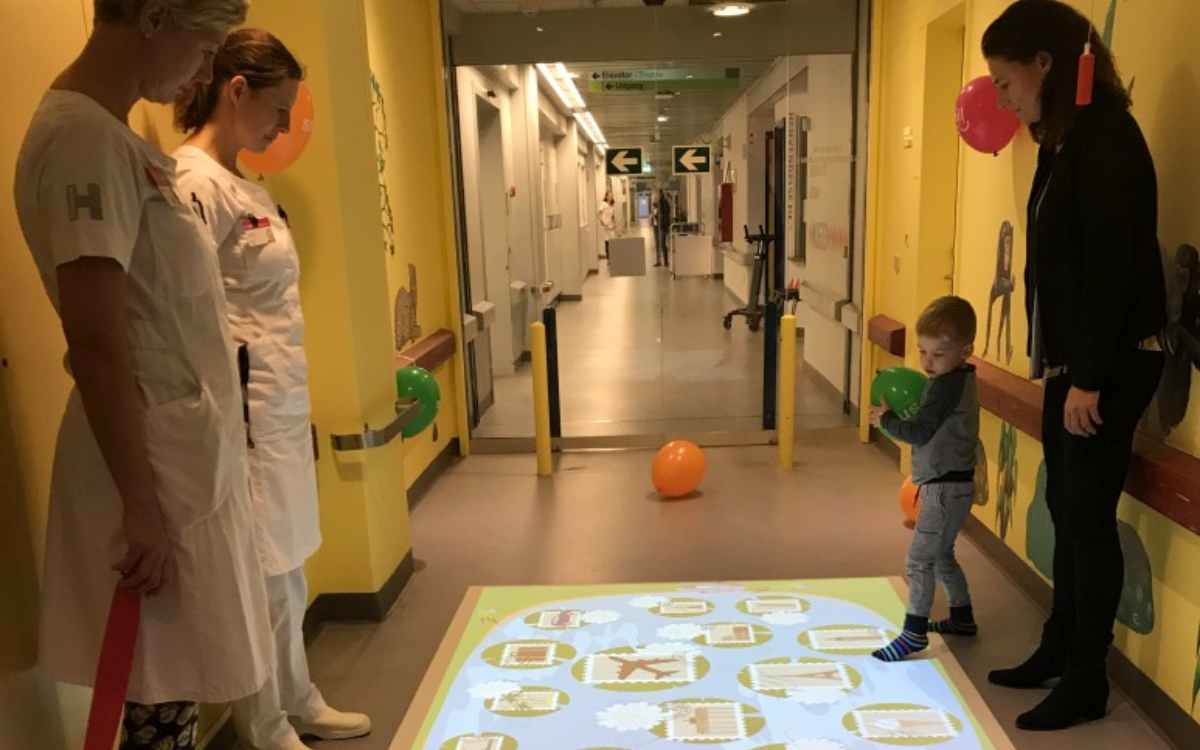 A young child in a hospital interacts with a colorful projected scene from an ActiveFloor Mobile Projector.