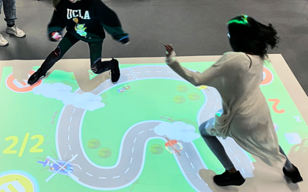 Children race around a projection from an ActiveFloor mobile projector, as they interact with dynamic visuals on the floor. 