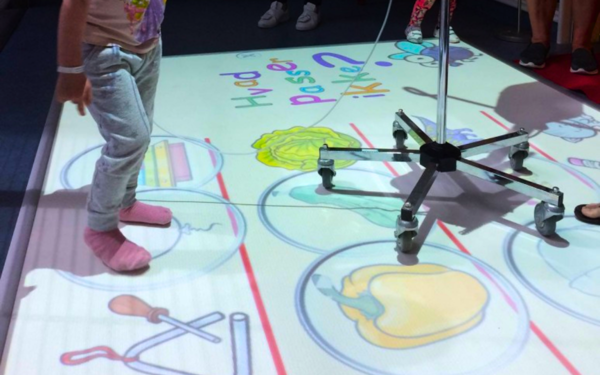 A young child in a hospital, connected to an IV drip, plays with an interactive scene projected onto the floor by an ActiveFloor Mobile Projector. 