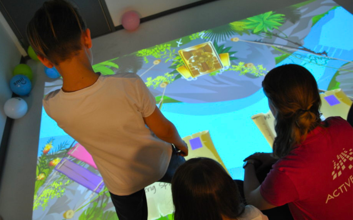 A group of young children in a hospital interacting with an immersive scene projected onto the floor by an ActiveFloor Mobile Projector. 